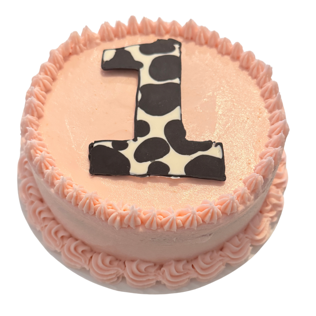 Round peach buttercream first birthday cake topped with a cow print number one